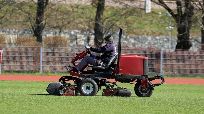 A person riding on a red lawn mower in a field.