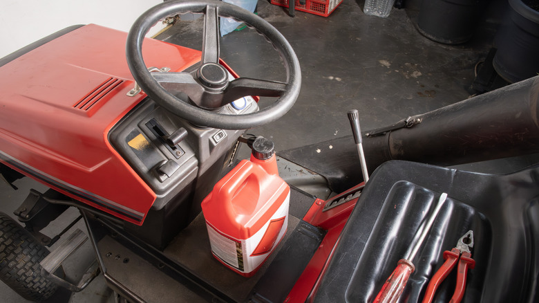 A riding lawn mower with a bottle of engine oil on the seat.