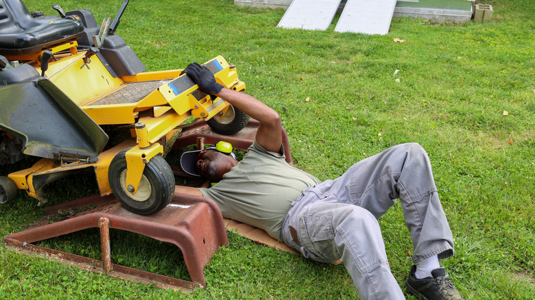 Man working under the deck of an old-school riding lawn mower.