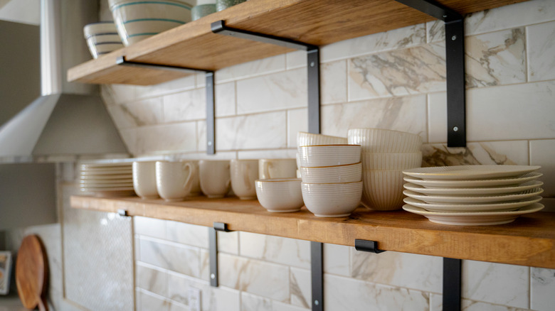 Two open kitchen shelves with a collection of dishes on them