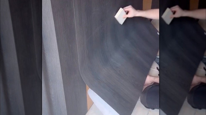 Person applying vinyl wrap to the sides of their golden wood kitchen cabinets