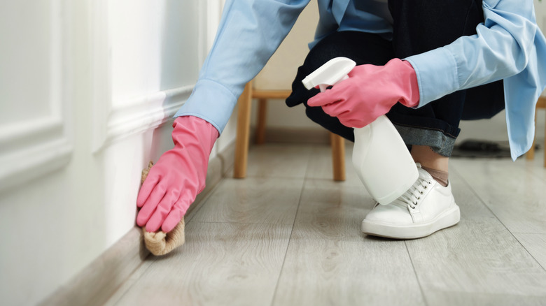 Person with spray bottle and cloth cleaning baseboards