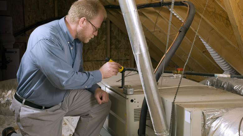 A person uses a flashlight to examine a heating system in an attic