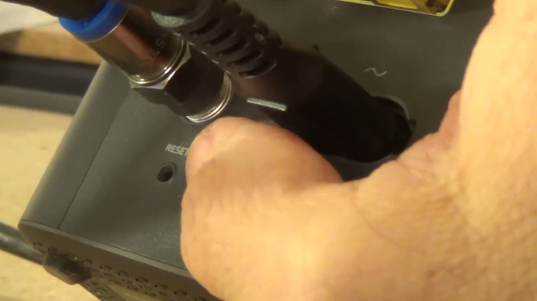 Thumb hovering over the reset button of an Xfinity modem