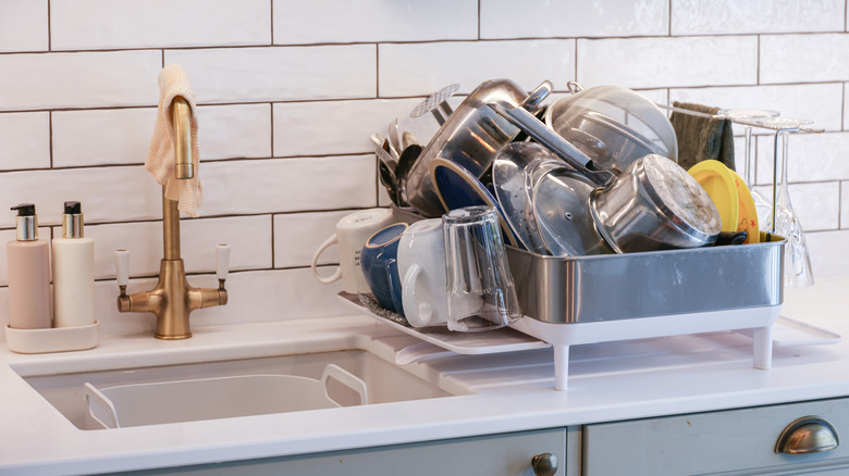 An overloaded dish drying rack is piled high with clean dishes
