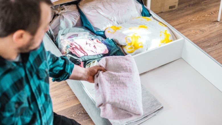A man puts folded linens in divided under-bed storage trundle