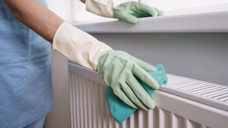 Gloved hands use a blue microfiber cloth to dust a wood wainscoting in a home.