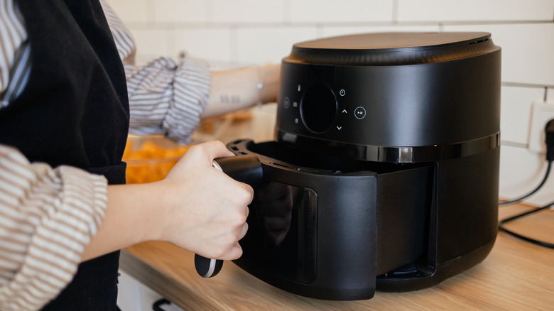 woman wearing a black apron using a black air fryer