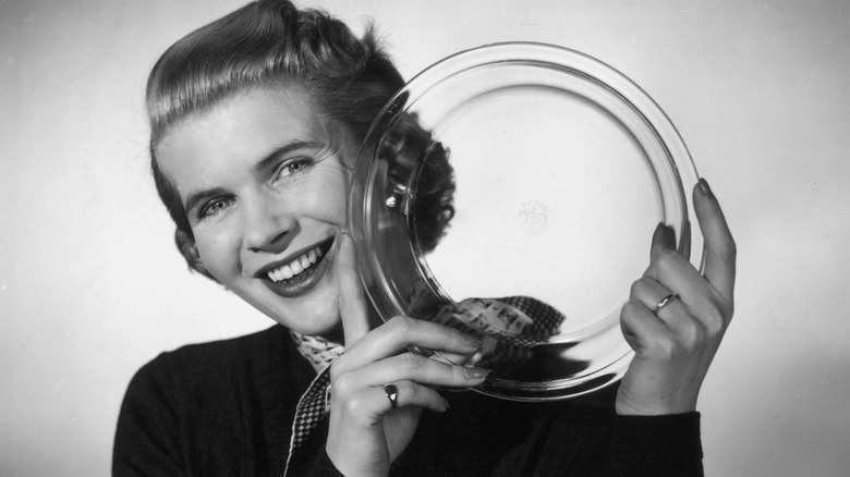 A woman holds up a Pyrex dish and smiles, black and white