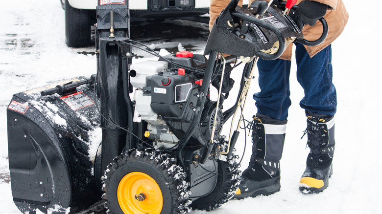 Close up of the complex workings of a snow blower, with a man prepared to start it.