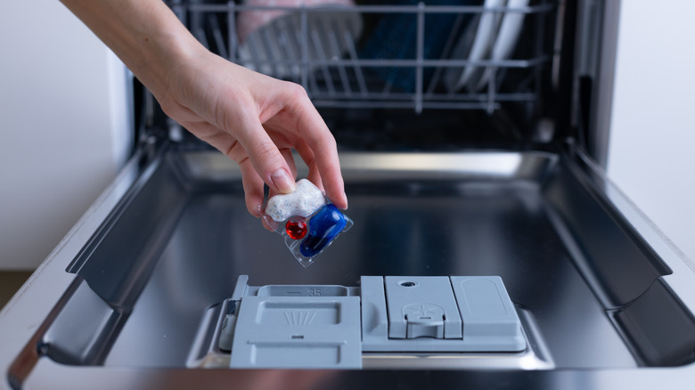Hand about to place a dishwasher detergent pod into the washer's compartment.