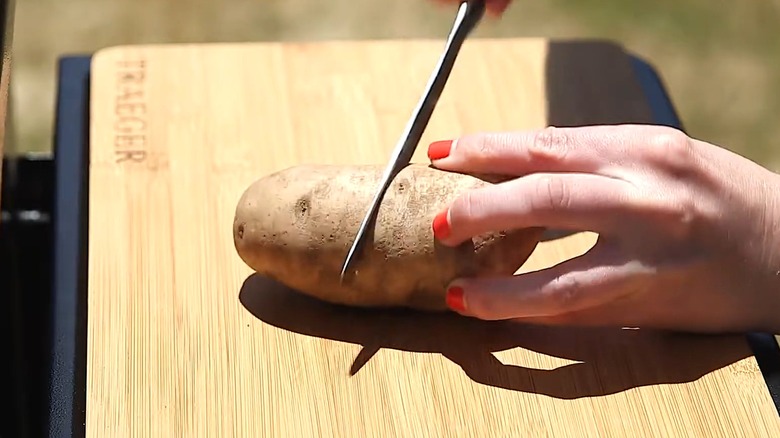 Person cutting raw potato on cutting board on gas grill shelf