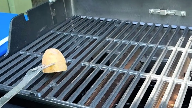 Person using a fork to rub a raw potato onto preheated grill grates