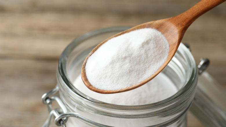An open jar of baking soda with a little on a wooden spoon
