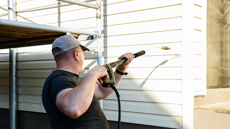 A man uses a high-powered pressure washer to clean vinyl siding