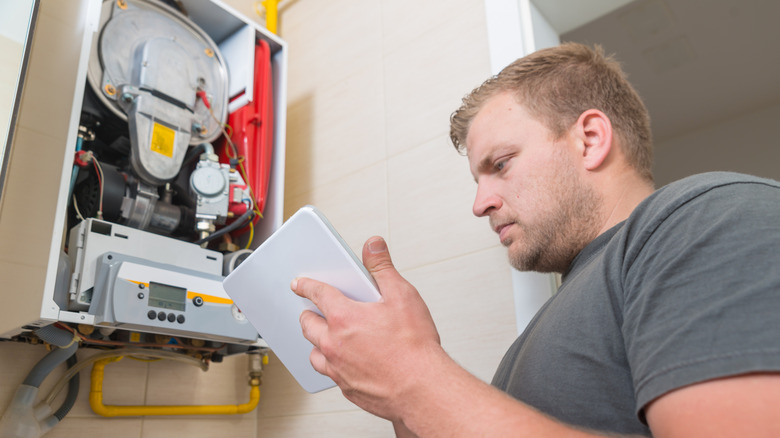 man with open furnace unit attempting to fix it while reading directions from a tablet