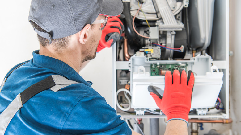 A repairman wearing red gloves tries to fix a residential furnace problem