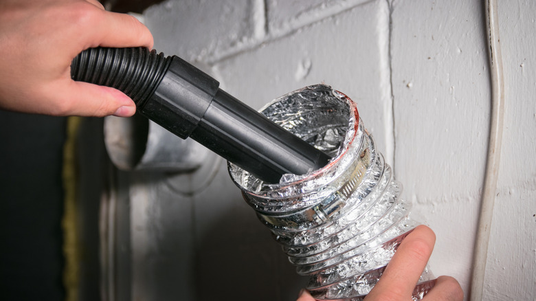 A person cleaning a dirty dryer vent with a vacuum