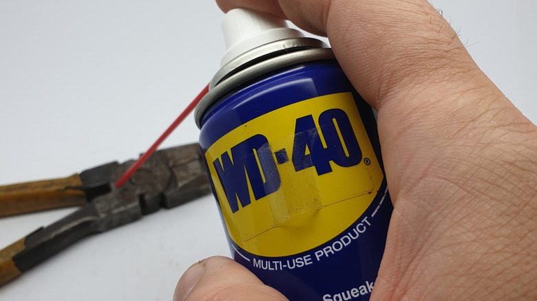 Someone spraying WD-40 onto a rusty tool