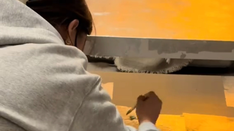 A person adds leafing adhesive to an IKEA table to prepare it for foil
