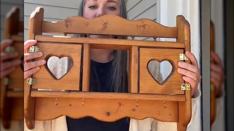 Woman holds up a wood shelf with hearts cut out of the doors