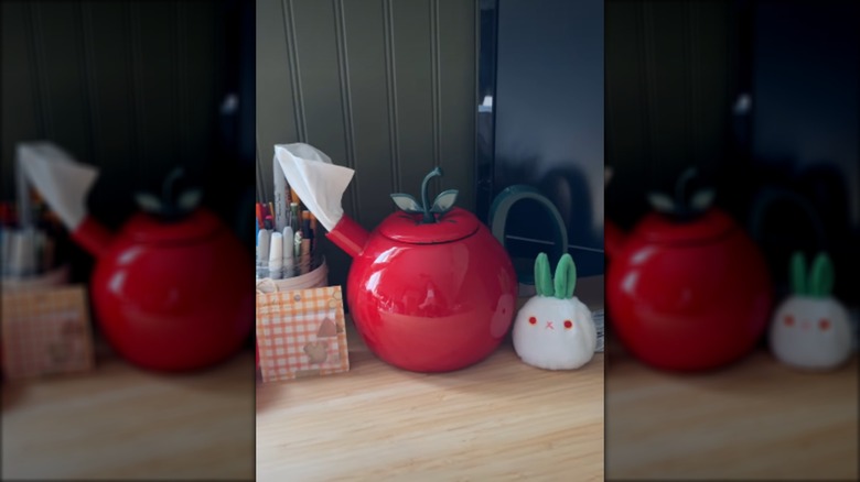 Apple-themed tea kettle being used as a tissue dispenser on a desk