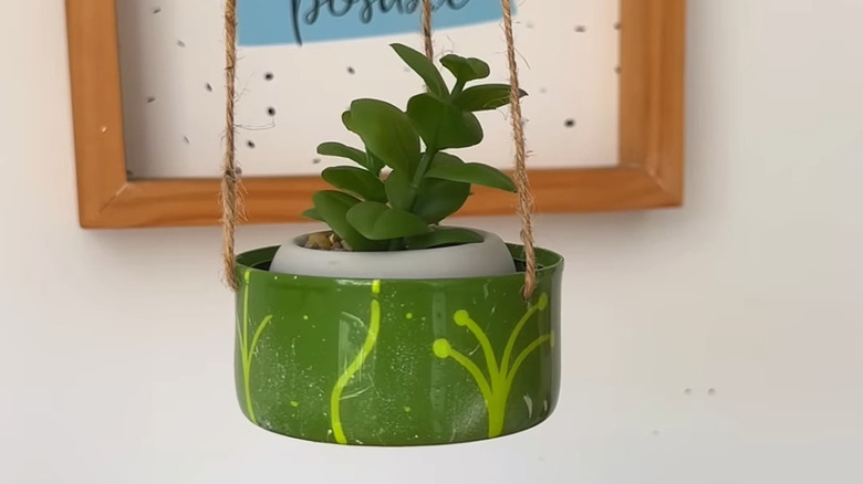 A green planter hanging with string and holding a succulent