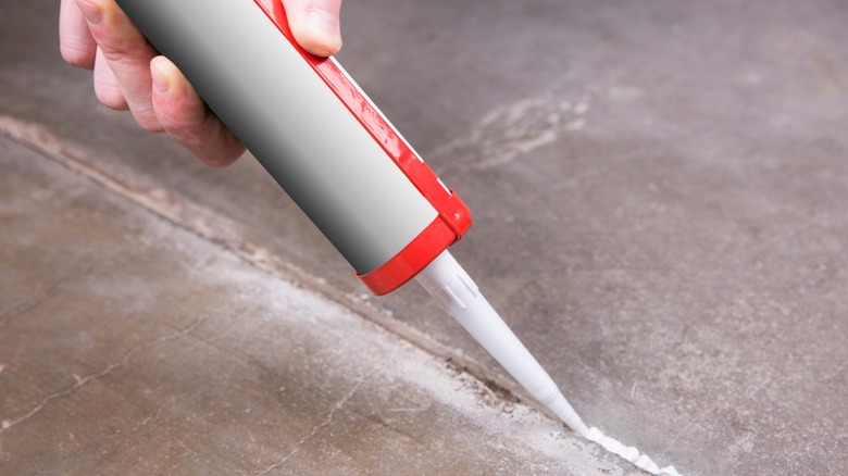 Hand holding caulk gun while filling a crack in concrete