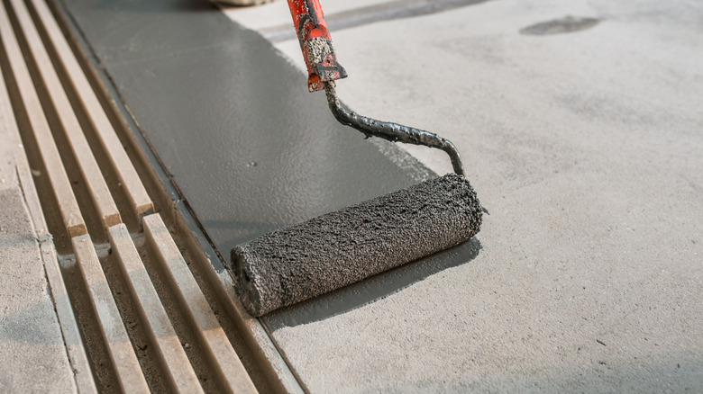 A paint roller painting a concrete floor in dark gray
