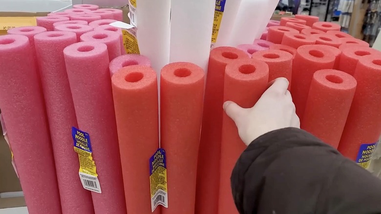 A hand is shown grabbing a red pool noodle from a floor display