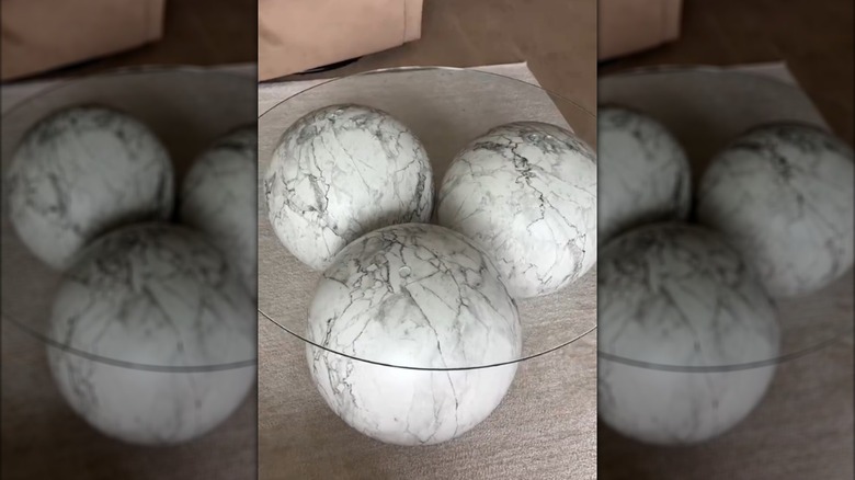 Glass coffee table with three marble balls as base in neutral-colored chic living room on beige carpet