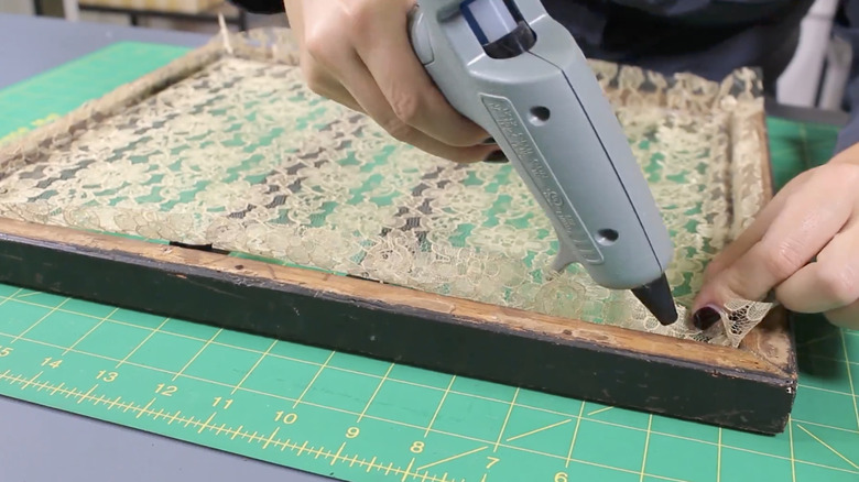 A person using a hot glue gun to affix the lace to a picture frame to make this craft.