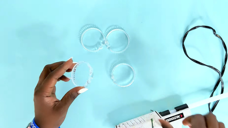 Creator holding a plastic shower curtain ring with a hot glue gun on the table