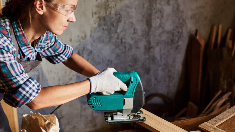 A person in a garage cutting wood with a jigsaw.