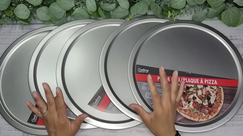 Woman's hands over a collection of Dollar Tree pizza pans for DIY project