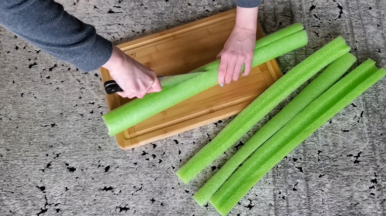 A woman cutting a green pool noodle in half