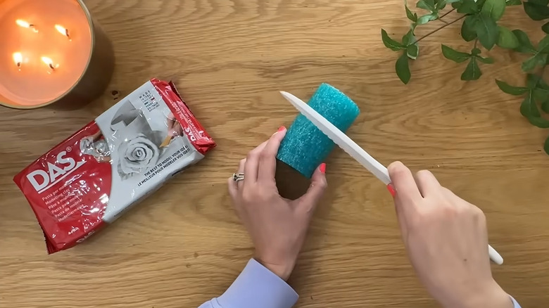 Creator cutting a pool noodle into a smaller section with air-dry clay and a candle on the table