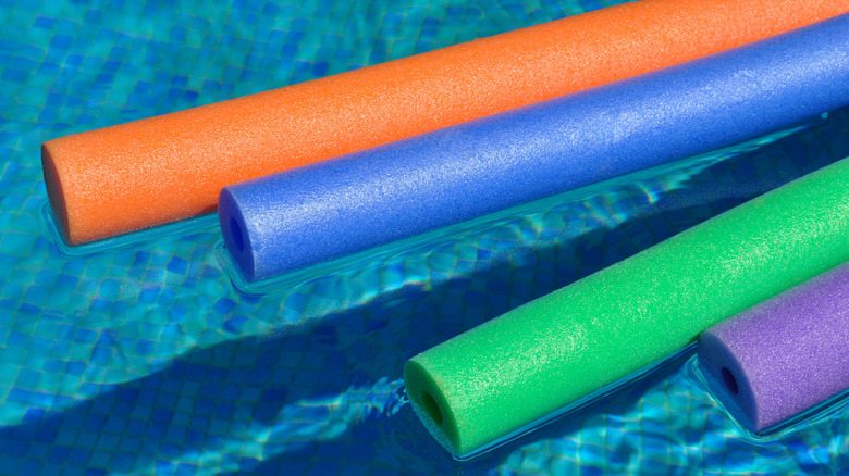 An orange, blue, green, and purple pool noodles floating in the pool.