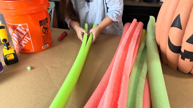Woman slicing pool noodles in half for fall DIY project on cardboard on worktable