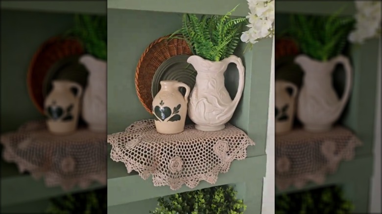 A green shelving unit decorated with a vintage doily and decor