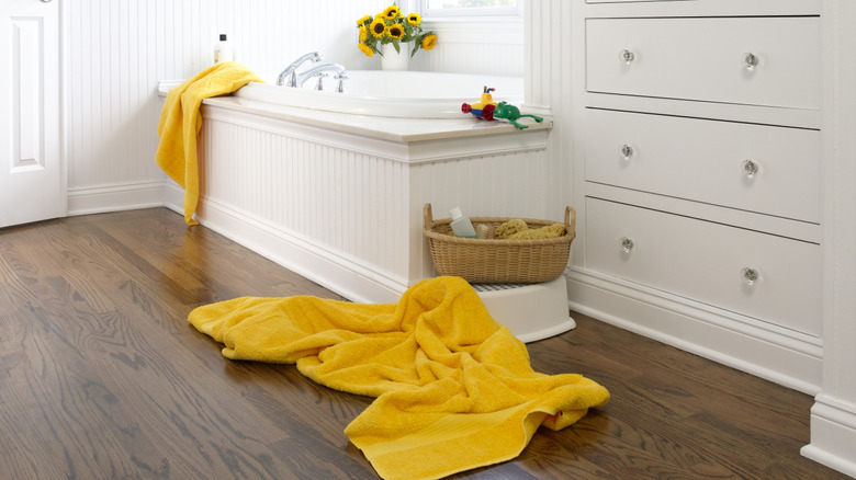 Yellow towels on a bathroom floor and draped over tub