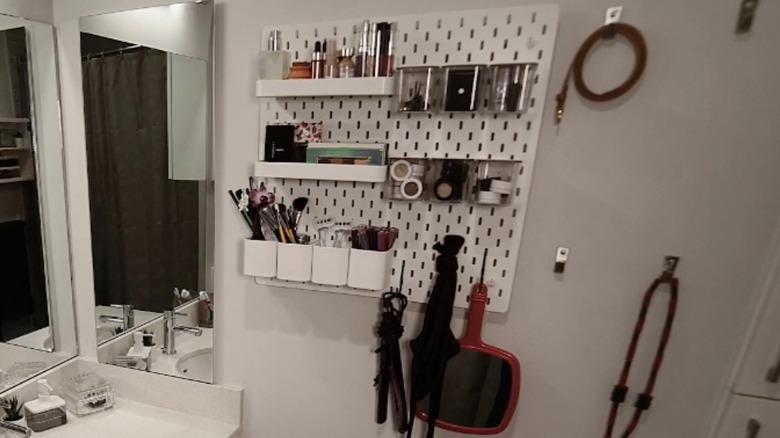 An IKEA SKÅDIS pegboard with attached accessories hanging on a bathroom wall