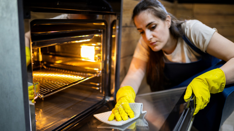 A cleaning lady wearing yellow gloves wipes an oven door