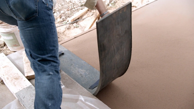 Chip Gaines using a rubber stamp on fresh concrete slab.