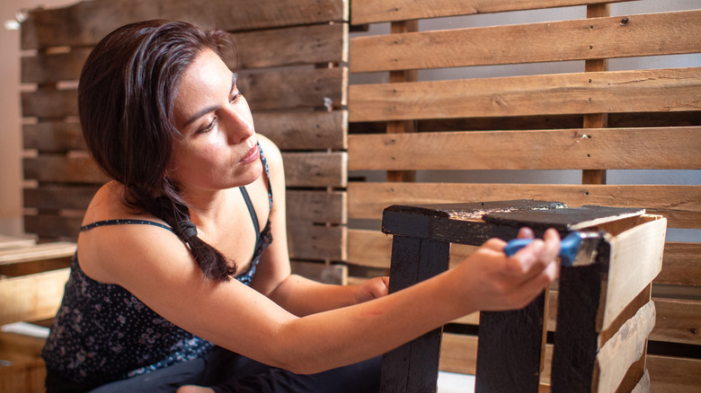 woman surrounded with wood pallets painting wood pallet box