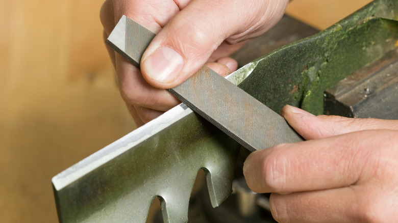 Using a file to sharpen a lawn mower blade