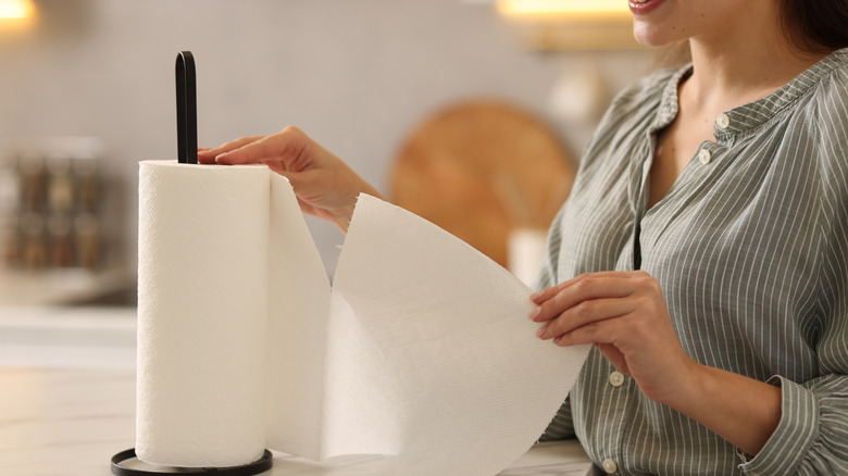 A woman tears a paper towel off a metal holder on a kitchen counter