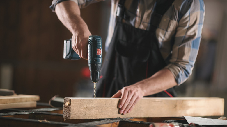 A person using a power drill on a wood post