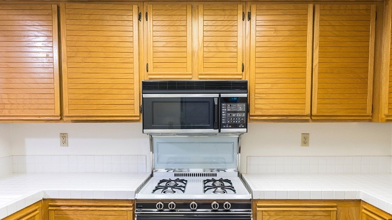 Kitchen cabinets over a gas range and OTR microwave in 1980s kitchen