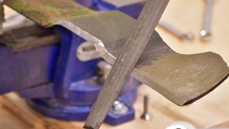 Using a file to sharpen a lawn mower blade